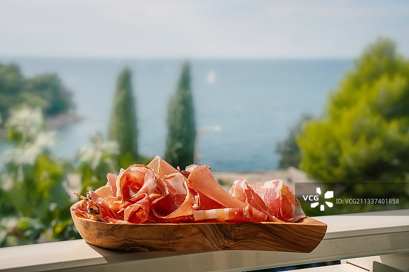 木盘上的薄切火腿，背景是湖泊和树木图片素材