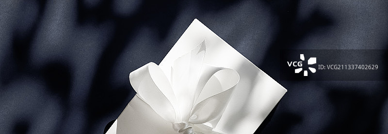 黑色背景上带有丝绸彩带和蝴蝶结的白色豪华节日礼品盒图片素材