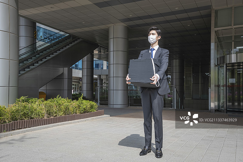 受疫情影响，亚洲男员工戴口罩，因裁员离开办公室并带走纸箱图片素材