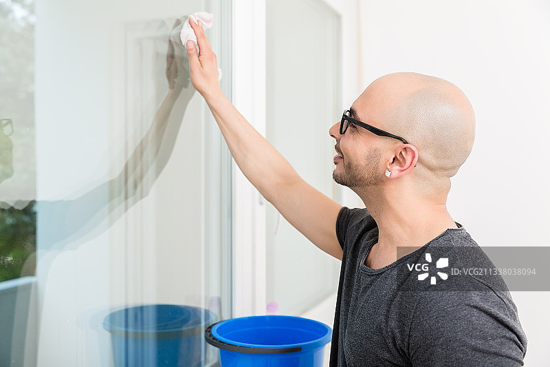 一个微笑的男人用白布擦窗户玻璃的特写图片素材