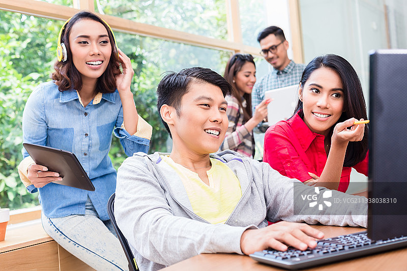 愉快的年轻员工在台式电脑上工作，同时听从他在办公室有经验的女同事的帮助指示图片素材