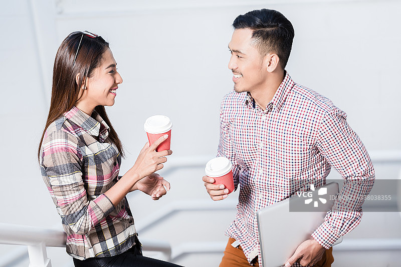 在工作的休息时间，快乐的年轻人和女人一边喝着一次性杯子里的咖啡一边聊天图片素材