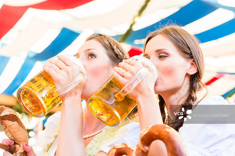 两个朋友在帐篷里的巴伐利亚民间集市上喝着啤酒杯里的啤酒图片素材