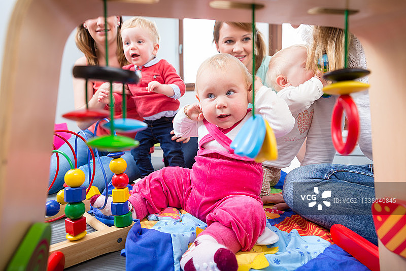 一个可爱的小女孩的肖像，看着她美丽的蓝眼睛，而坐在地板上与其他两个婴儿和他们的母亲在家里图片素材