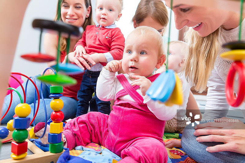 一个可爱的小女孩的肖像，看着她美丽的蓝眼睛，而坐在地板上与其他两个婴儿和他们的母亲在家里图片素材
