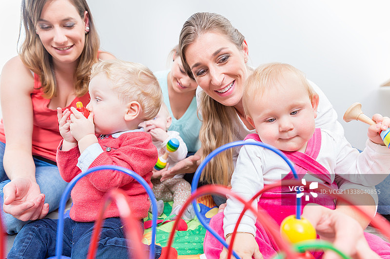 一群快乐的年轻母亲看着他们可爱和健康的婴儿，同时玩五颜六色的玩具在一个现代日托中心图片素材
