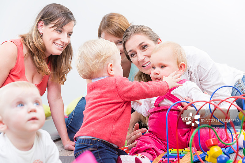 一群快乐的年轻母亲看着他们可爱和健康的婴儿，同时玩五颜六色的玩具在一个现代日托中心图片素材