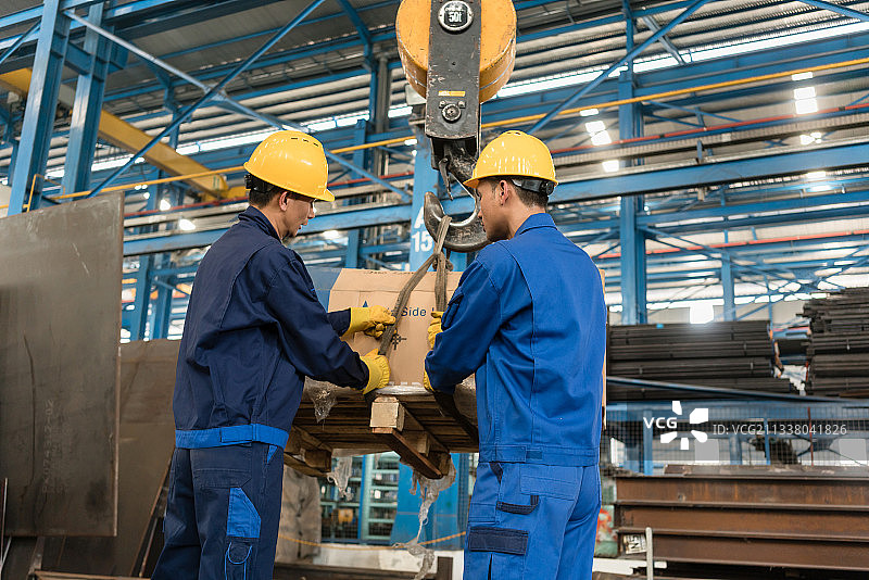 在一家冶金厂的内部，两名亚洲工人正在用起重机搬运重物图片素材