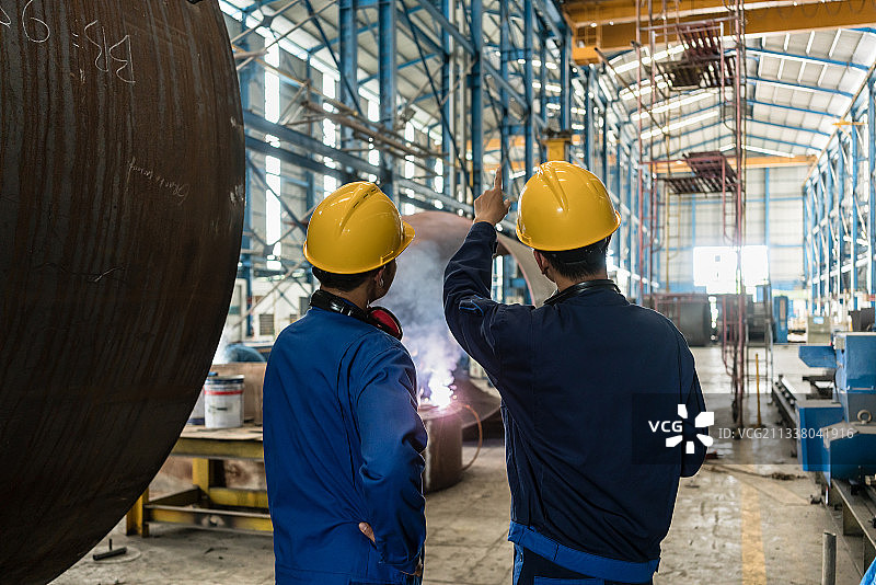 两位亚洲专家一边在室内监督工业锅炉的制造一边交谈图片素材