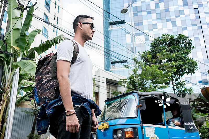 低角度的侧视图，一个年轻男子戴着太阳镜和背包在印度尼西亚的街道度假图片素材