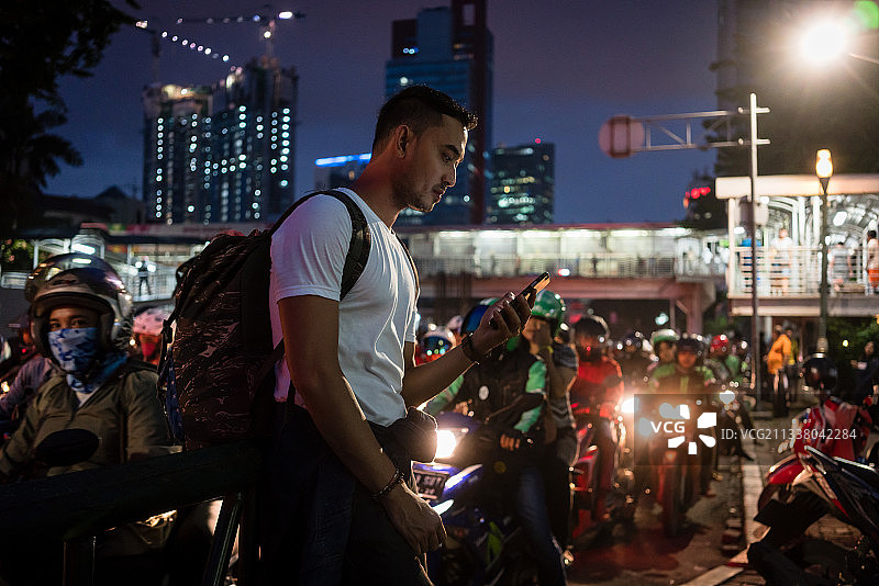 雅加达，一名年轻男性游客在晚上走在拥挤的街道上，旁边有骑摩托车的人图片素材