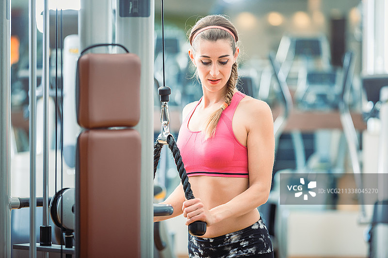 快乐和美丽的fit女人穿着粉红色的健身胸罩，同时在健身房锻炼缆绳三头肌伸展图片素材