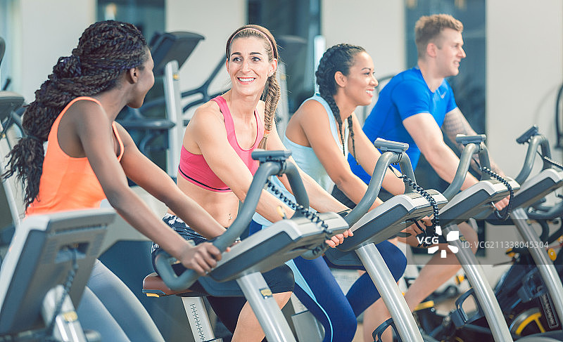 黑发美丽的女人微笑，而骑现代健身自行车在团体动感单车课在健身房图片素材