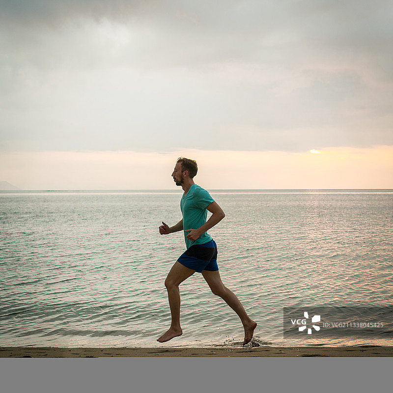 全长侧面的一个运动的年轻男子在海滩上跑步在暑假期间的有氧运动在印度尼西亚图片素材