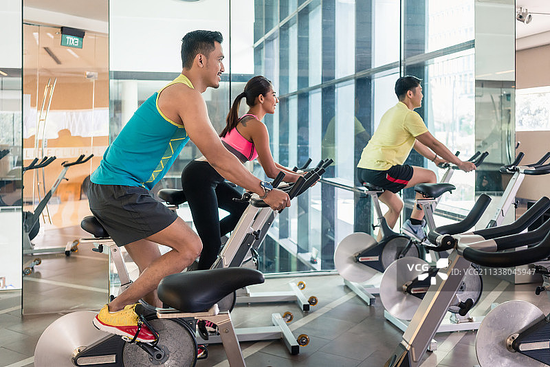 在一家现代健身俱乐部的HIIT室内自行车课上，帅气自信的年轻人微笑着骑自行车图片素材