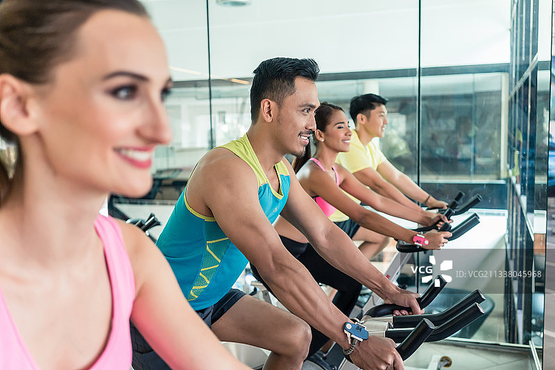 侧面的美丽的健康年轻的女人微笑，而在一个现代健身俱乐部的室内自行车组在有氧运动图片素材