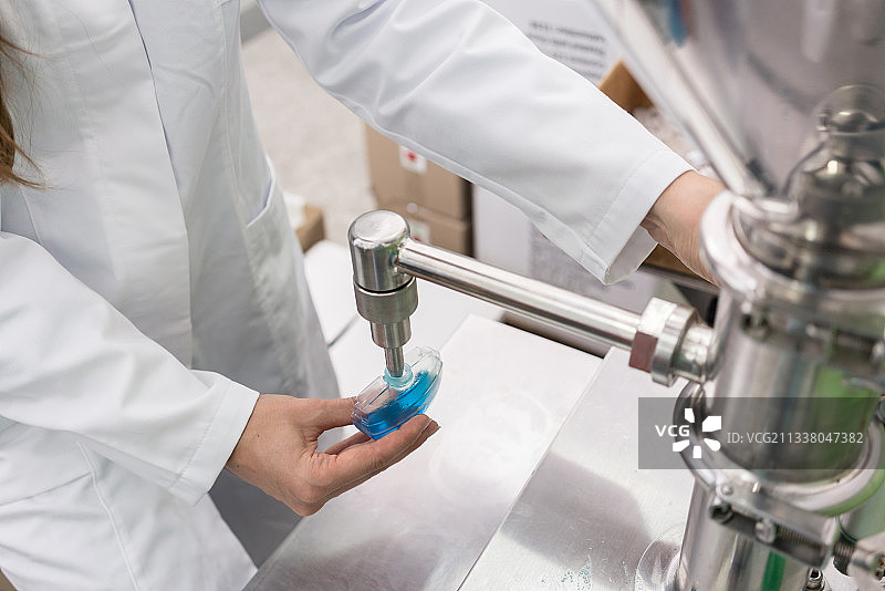侧视图特写的一个女性技术员的手填充塑料容器与液体物质，为实验室测试期间的质量控制在化妆品工厂图片素材