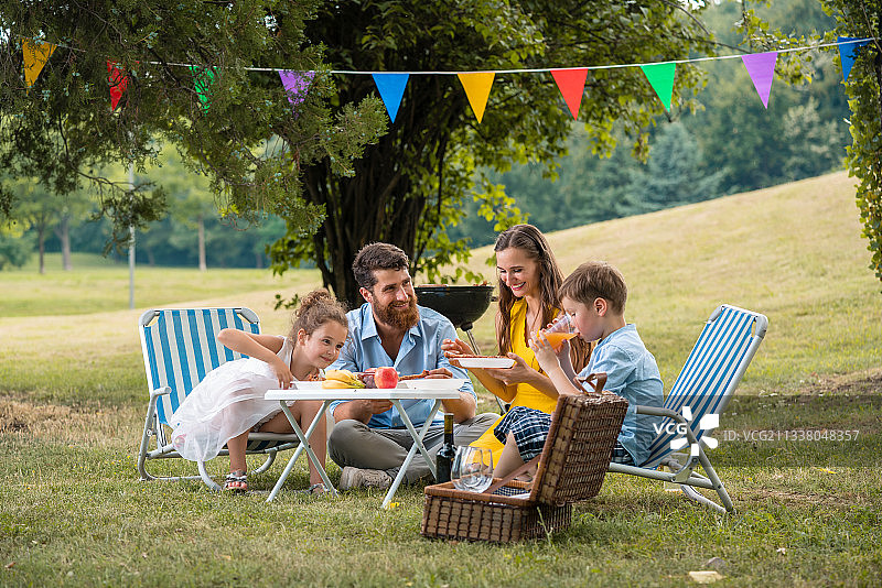 专注的年轻父母两个孩子听他们有趣的儿子说话，同时在一起吃在一个夏天的家庭野餐图片素材