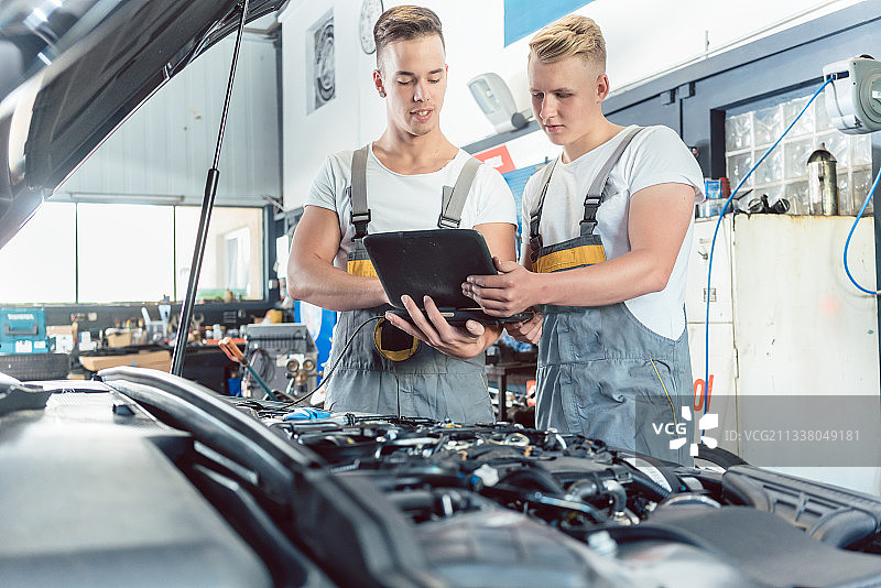 在一家现代汽车修理厂，有经验的汽车修理工在一个学徒旁边用笔记本电脑扫描和解释引擎错误代码图片素材