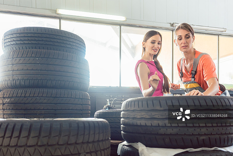 在一家出售各种轮胎的汽车修理店，有经验的女性汽车修理工正在为顾客检查轮胎的识别号图片素材