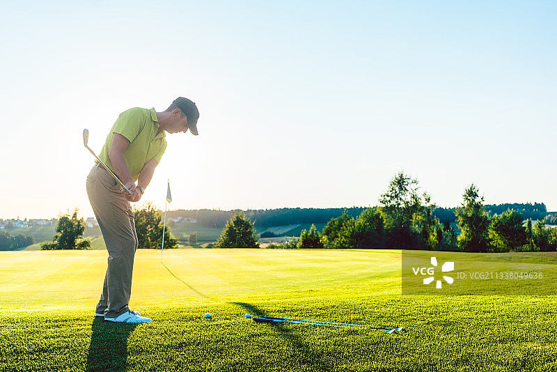 一个经验丰富的男性高尔夫球手的全长后视图打高尔夫球对杯子，在高尔夫球场在一个专业的个人比赛在夏天图片素材