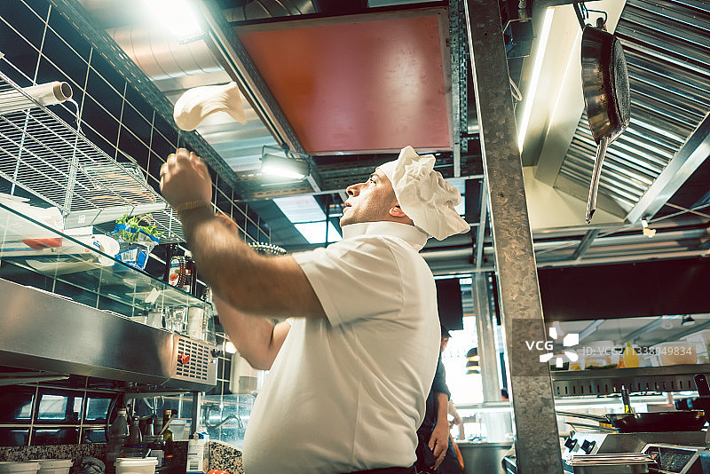 一个经验丰富的厨师在一个现代意大利餐厅的厨房里准备披萨时扔面团的低角度的侧视图图片素材