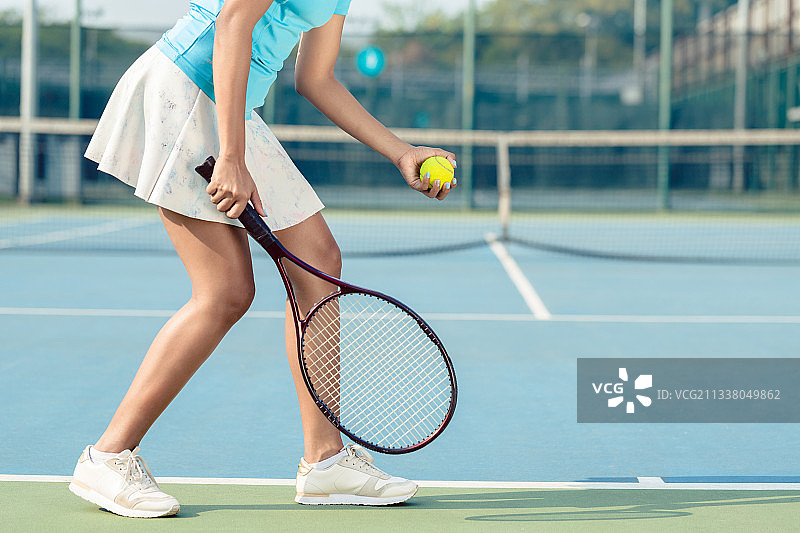 在职业比赛发球时，穿着白色裙子和网球鞋的年轻女子的侧视图图片素材