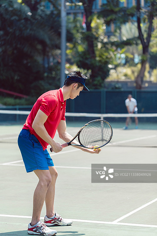 在专业网球场上，一名亚洲网球运动员在双打混合比赛开始时准备发球的侧视图图片素材