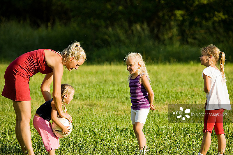 母亲带着三个女儿在阳光普照的绿色草地上踢足球(好吧，是北美足球)图片素材