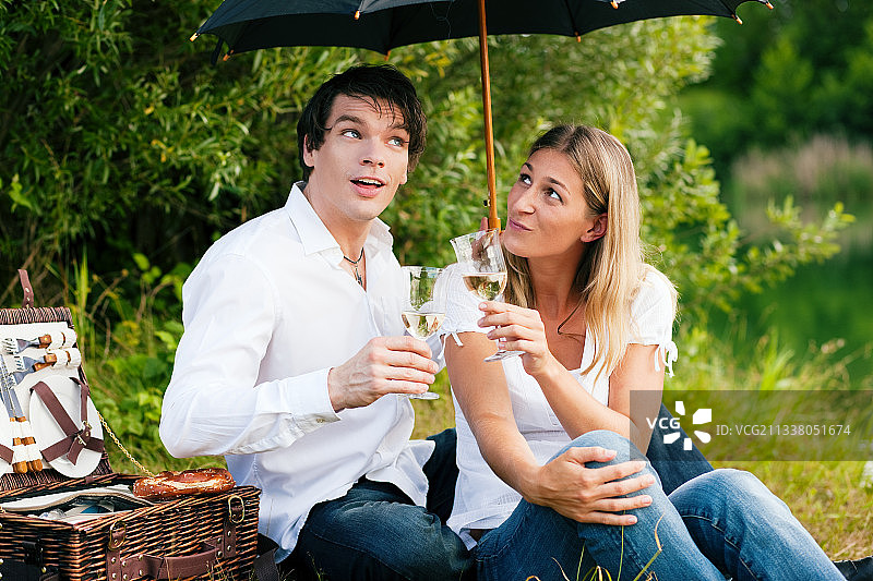 一对相爱的情侣坐在湖边，带着酒野餐——天开始下雨了，但他们不太在意图片素材