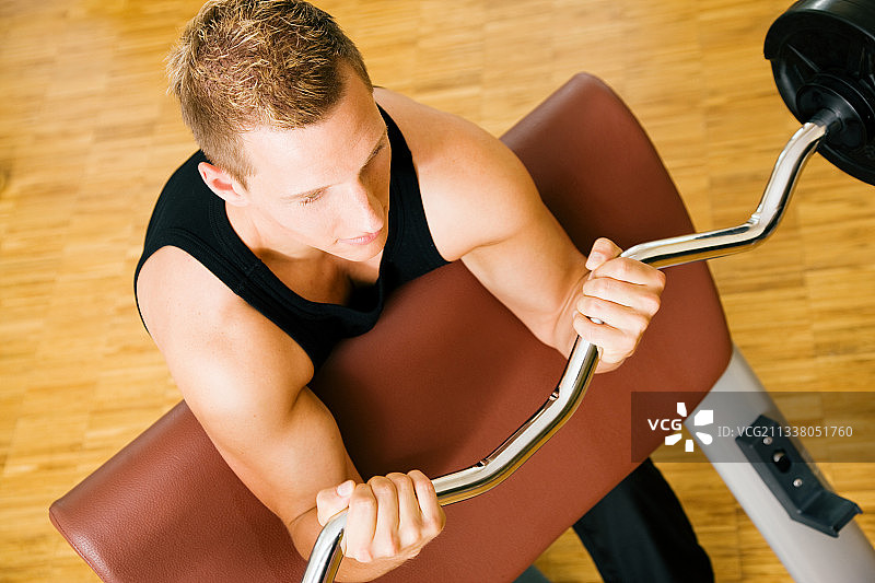 一个年轻人(抬起头)正在健身房用杠铃进行训练图片素材