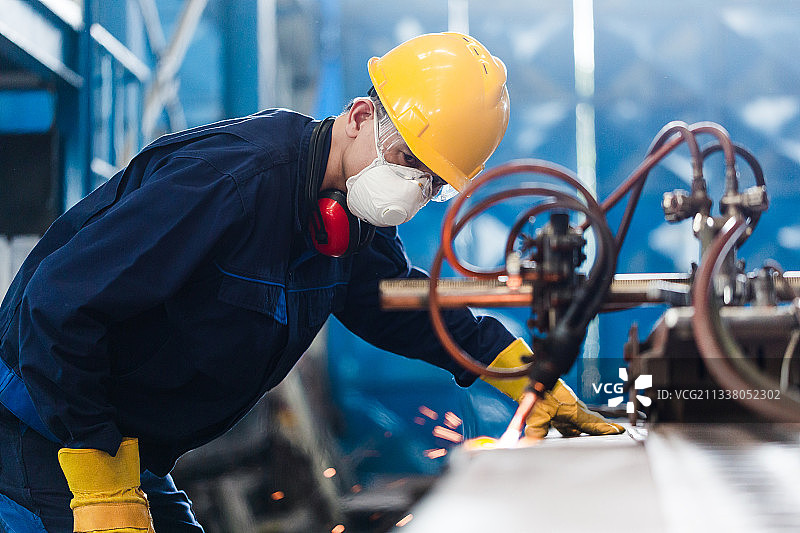 亚洲工人在使用数控等离子切割机时佩戴防护装备图片素材