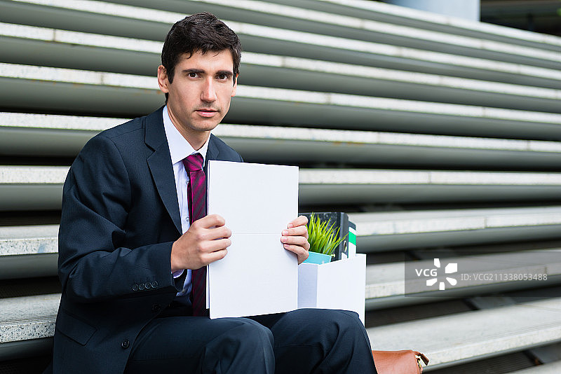 失业的年轻人在被解雇或企业破产后坐在户外的楼梯上，带着悲伤的表情看着镜头图片素材