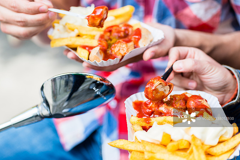 一男一女骑着摩托车吃德国特色咖喱香肠和炸薯条图片素材