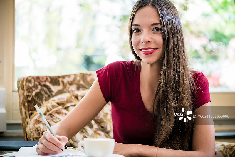 年轻女子看着相机，在咖啡馆里写作图片素材