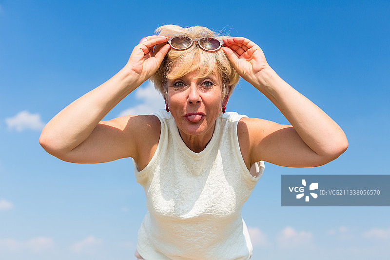 肖像的一个有趣的妇女伸出她的舌头，而摆姿势在户外的蓝天在一个阳光明媚的夏天图片素材