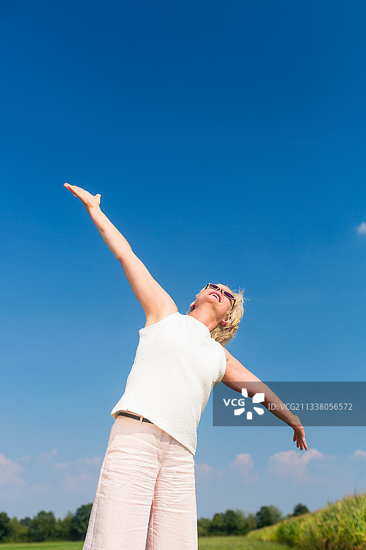 低角度的一个健康的妇女仰望天空与伸开的胳膊，而享受退休在一个阳光明媚的夏天图片素材