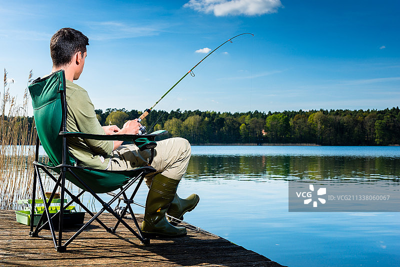 在湖边钓鱼的人坐在靠近水的码头上图片素材