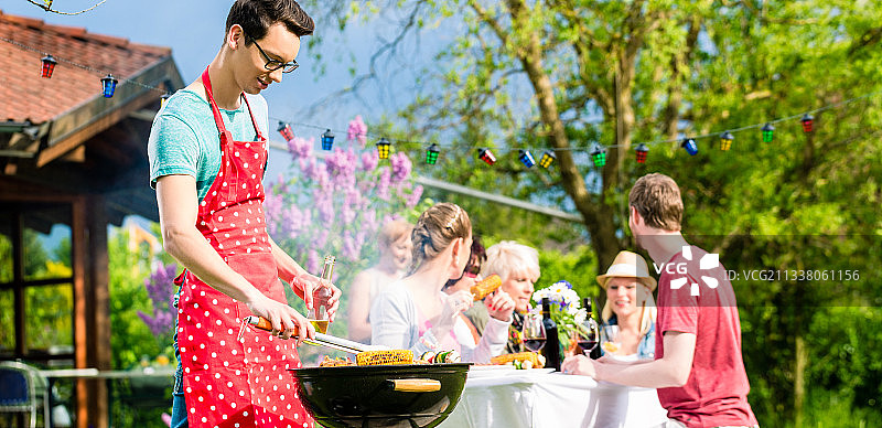 男子在花园烧烤派对上烤肉，背景是朋友们吃喝图片素材