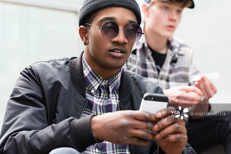 时尚的年轻男孩用手机和他的朋友在背景图片素材