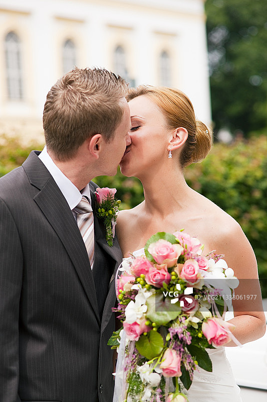 婚礼上，新郎在公园里亲吻新娘，她手里捧着一束鲜花图片素材