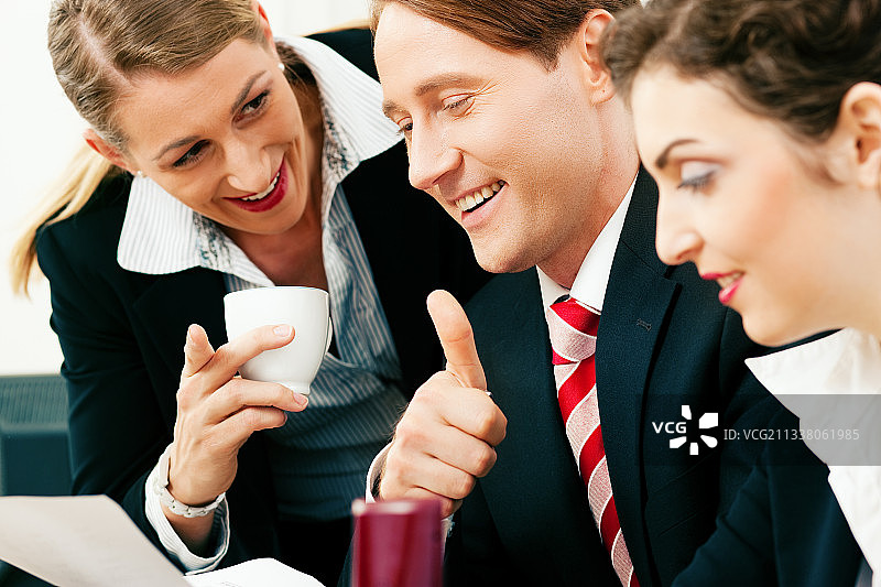 一个小的商业团队——男人和两个女人——在办公室里工作很成功，一个女人喝着一杯咖啡图片素材