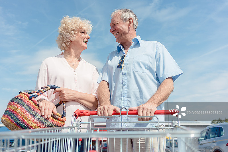 低角度的肖像，一个活跃的老人抱着一个购物推车，而看着他的妻子与爱对着蓝天图片素材