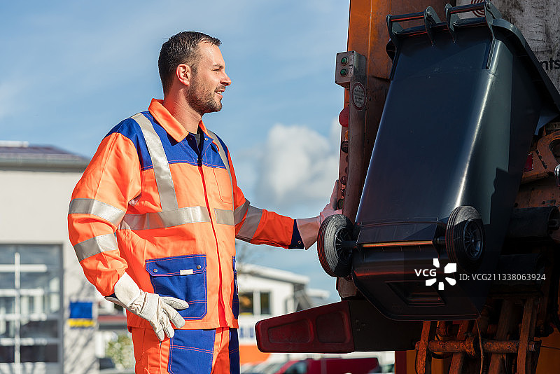 垃圾收集工人将垃圾桶放入垃圾车中进行清理图片素材