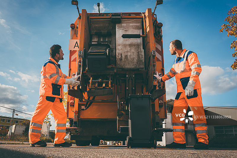 两名垃圾收集工人将垃圾装进垃圾车，倒空货柜图片素材