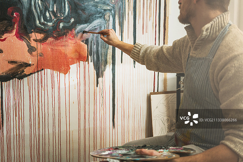 自信的男性艺术家拿着调色板和油漆刷在画室板上画抽象画图片素材