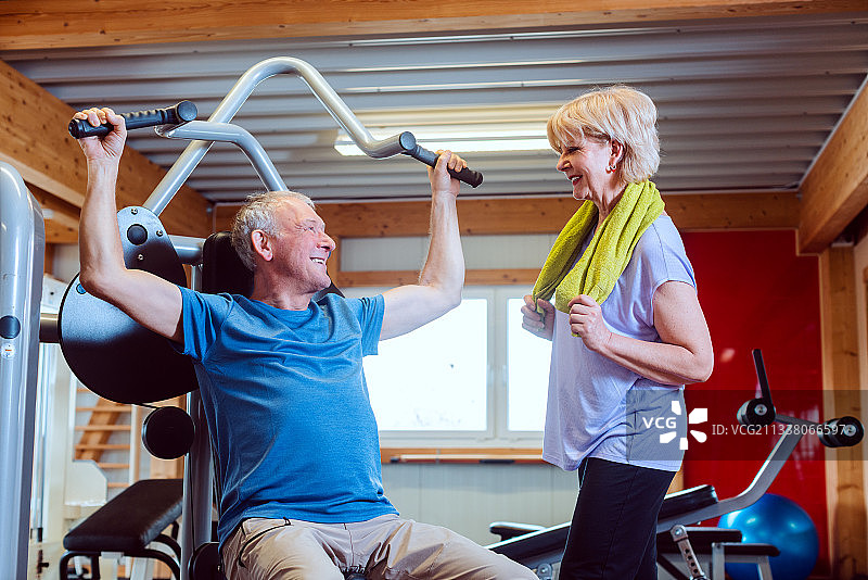 快乐的老人在健身房和他的妻子在健身机上图片素材