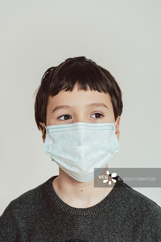 2019冠状病毒病危机期间戴口罩在家的小男孩图片素材