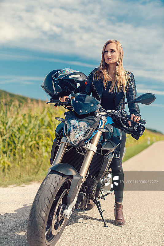 美丽的女人骑着摩托车看着前方的道路在夏天的一天图片素材