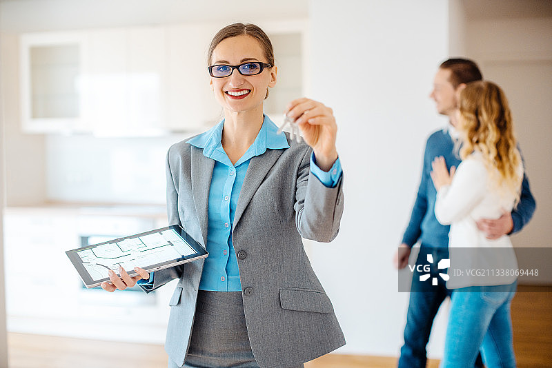 公寓经纪人拿着新房子的钥匙和平面图，客户站在后面图片素材